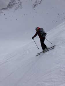 Side view of a skier wearing a backpack heading down a snowy run. 