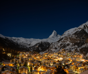 View of the cozy ski town of Zermatt at night in winter. The Matterhorn is visible in the distance silhouetted against a clear sky.