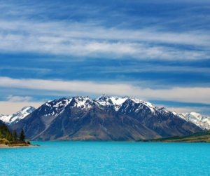 Looking out across the turquoise waters of Lake Ohau in New Zealand to a snowy mountain in the distance.