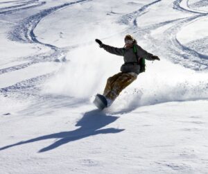 A snowboarder carving turns with his hands outstretched on a sunny day.