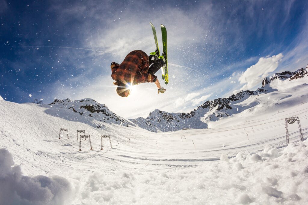 A skier upside down mid-flip backdropped by the sun on a bright, sunny day.